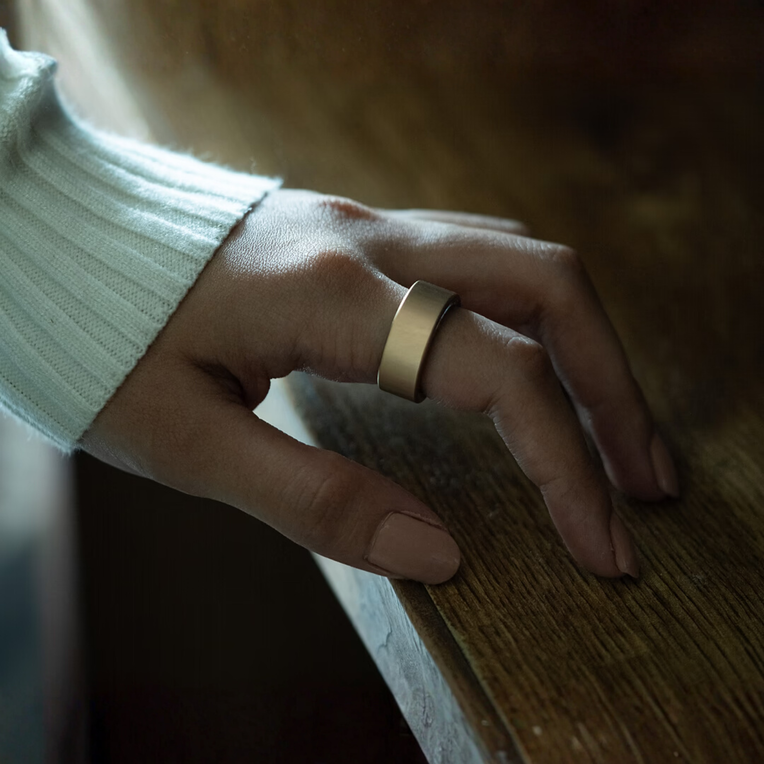 Hand wearing a gold ring on a wooden surface