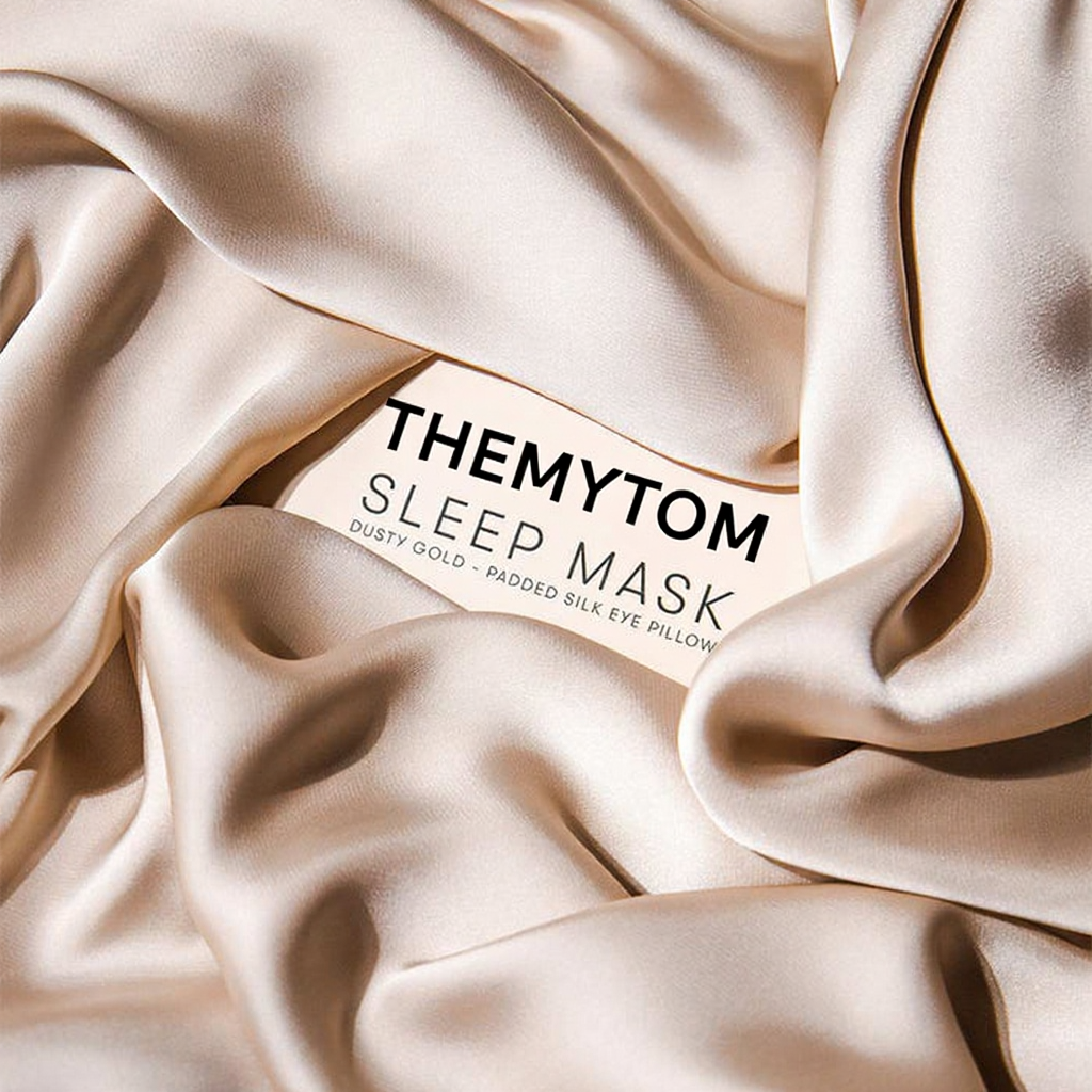 Silky sleep mask with 'THEMYTOM' branding on a beige fabric background Nº 12 Éclat de Rose Nº 08 Brume d’Argent Nº 21 Ombre Noire Nº 14 Bleu Céleste